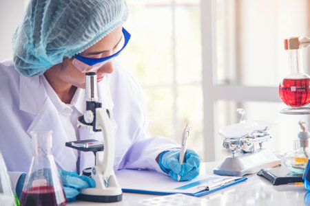 Asian Woman scientist hand write note research in medical lab look at science microscope medical test. Researcher biology chemistry. Asian Female technician laboratory using microscope blood testの写真素材