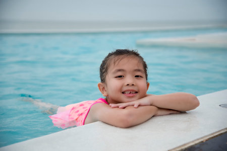 Toddler girl Kid swim playful in swimming pool summer time with pink swimwear in blue water at hotel swimming pool outdoor. Happy girl swim playful water splash with happiness on summer vacationの写真素材