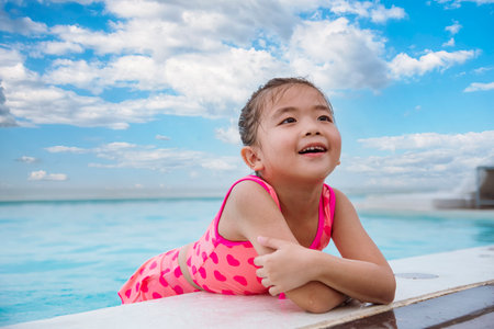 Portrait Girl in pink swimsuit playful in swimming pool summer time with pink swimwear, blue water at hotel swimming pool outdoor. Toddler girl Kid smile laugh look at camera. Happy girl swim playfulの写真素材
