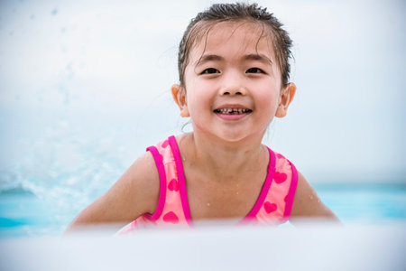 Portrait Toddler girl Kid smile laugh look at camera. Girl in pink swimsuit playful in swimming pool summer time with pink swimwear, blue water at hotel swimming pool outdoor. Happy girl swim playfulの写真素材