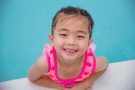 Portrait Toddler girl Kid smile laugh look at camera. Girl in pink swimsuit playful in swimming pool summer time with pink swimwear, blue water at hotel swimming pool outdoor. Happy girl swim playfulの写真素材