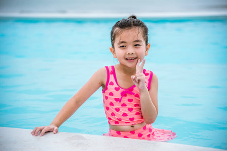 Portrait Toddler girl Kid smile laugh look at camera. Girl in pink swimsuit playful in swimming pool summer time with pink swimwear, blue water at hotel swimming pool outdoor. Happy girl swim playfulの写真素材