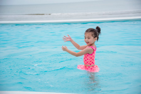 Toddler girl Kid swim playful in swimming pool summer time with pink swimwear in blue water at hotel swimming pool outdoor. Happy girl swim playful water splash with happiness on summer vacationの写真素材