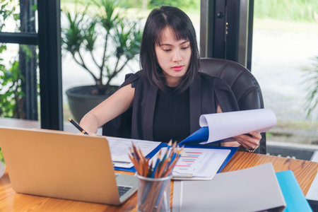 Business woman using smartphone, laptop on office desk. Female freelance reading financial graph charts Planning analyzing marketing data. Hands of young woman working in office firm business info.の写真素材