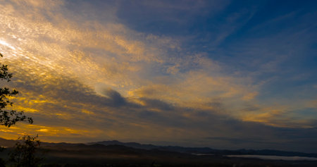 Blue golden sky sunrise dramatic beautiful landscape mountain. Dawn sky gold dusk time cloudscape with sunlight. Dramatic sunset over mountain landscape. Beautiful landscape foggy hills twilight timeの写真素材