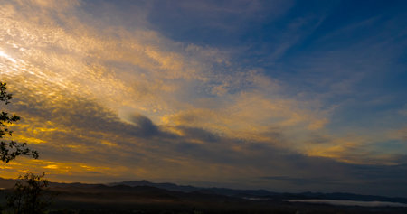 Blue golden sky sunrise dramatic beautiful landscape mountain. Dawn sky gold dusk time cloudscape with sunlight. Dramatic sunset over mountain landscape. Beautiful landscape foggy hills twilight timeの写真素材