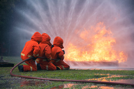 Firefighter Rescue team training in fire fighting extinguisher. Firefighter teamwork fighting with flame using fire hose chemical water foam spray engine. Fireman wear hard hat, safety suit uniformの写真素材