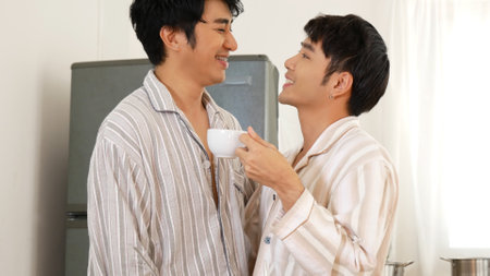 Happy gay couple enjoy breakfast in kitchen drinking coffee. Two best friends LGBTQ relation partner home cooking. Happiness romance homosexual marriage lifestyle. Two men together love friendship.の写真素材