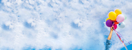 Banner Cheerful cute girl holding balloons running green meadow white cloud and blue sky with happiness. Panorama Hands holding vibrant air balloons happy times summer sunlight outdoor copy spaceの写真素材