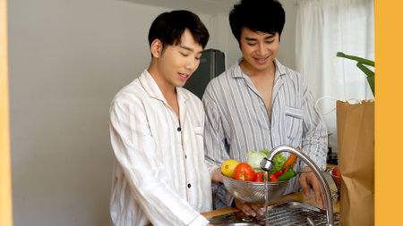 Happy Asian gay couple homosexual cooking together in kitchen wash vegetable organic salad healthy home cook. Asian two Man hands wash cleaning fresh vegetable in kitchen.  LGBTQIA lifestyle conceptの写真素材