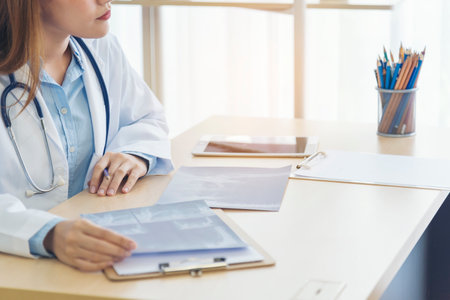 Close up hands of women doctor write prescription medical lab hospital. Crop asian women hand doctors working in medical clinic looking CAT scan xray film. Doctor with stethoscope writing on notepadの写真素材
