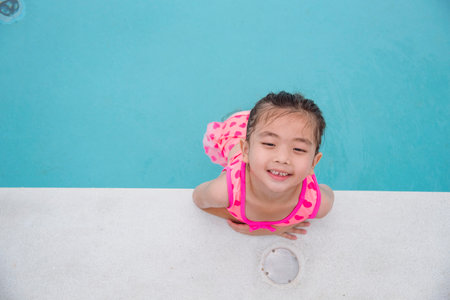 Portrait Girl in pink swimsuit playful in swimming pool summer time with pink swimwear, blue water at hotel swimming pool outdoor. Toddler girl Kid smile laugh look at camera. Happy girl swim playfulの写真素材