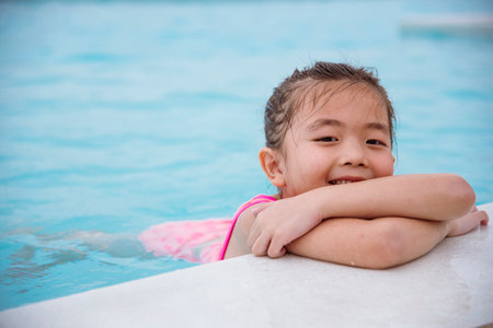 Toddler girl have fun swimming pool summer time with swimwear in blue water at hotel swimming pool outdoor. Kid swim playful water splash with happiness on summer vacation. Happy girl swim conceptの写真素材