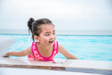 Toddler girl Kid swim playful in swimming pool summer time with pink swimwear in blue water at hotel swimming pool outdoor. Happy girl swim playful water splash with happiness on summer vacationの写真素材