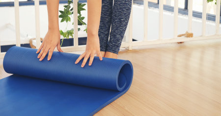 Woman hands rolled up yoga mat on gym floor in yoga fitness training room. Home workout woman close up hands rolling foam yoga gym mat. Woman barefoot home workout sportive healthy lifestyle conceptの写真素材