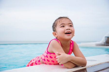 Toddler girl have fun swimming pool summer time with swimwear in blue water at hotel swimming pool outdoor. Kid swim playful water splash with happiness on summer vacation. Happy girl swim conceptの写真素材