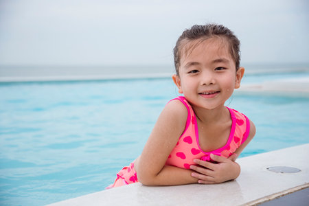 Toddler girl have fun swimming pool summer time with swimwear in blue water at hotel swimming pool outdoor. Kid swim playful water splash with happiness on summer vacation. Happy girl swim conceptの写真素材