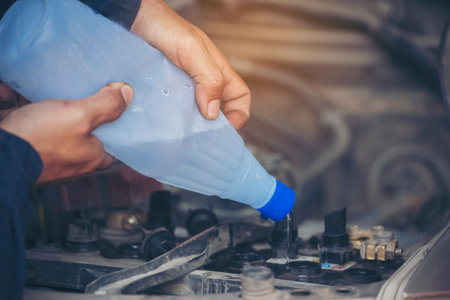 Car Mechanic man hands pouring Deionized purified Distilled water for car battery mechanical service. Close up hands man hold Deionized Distilled liquid water bottle at garage auto mobile car serviceの写真素材