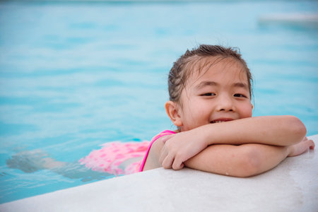 Toddler girl Kid swim playful in swimming pool summer time with pink swimwear in blue water at hotel swimming pool outdoor. Happy girl swim playful water splash with happiness on summer vacationの写真素材