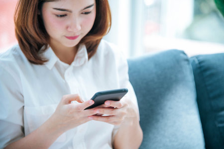 Asian woman holding smartphone with E-commerce Shopping online website Reading Online Article, Blog, vlog. Young Woman hands holding phone technology lifestyle. Happy Woman using digital smart phoneの写真素材