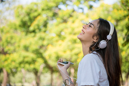 Leisure cheerful wellness woman Concept. Happy teenage woman listening to music wear headphones from smartphone outdoor in the park. Music mental therapist for wellness woman.の写真素材