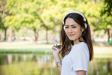 Leisure cheerful wellness woman Concept. Happy teenage woman listening to music wear headphones from smartphone outdoor in the park. Music mental therapist for wellness woman.の写真素材