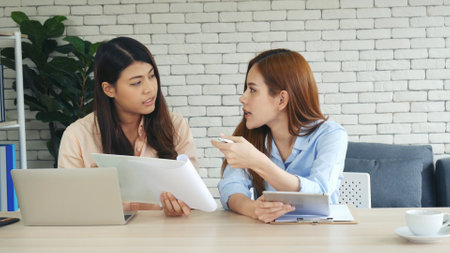 Two businesswomen team meeting using laptop at company office desk. Two young Female freelance reading financial graph charts Planning analyzing marketing data. Asian people team working office firm.の写真素材