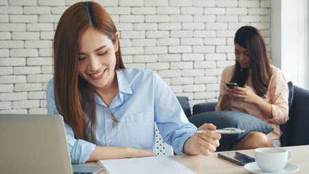 Two businesswomen team meeting using laptop at company office desk. Two young Female freelance reading financial graph charts Planning analyzing marketing data. Asian people team working office firm.の写真素材