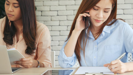 Two businesswomen team meeting using laptop at company office desk. Two young Female freelance reading financial graph charts Planning analyzing marketing data. Asian people team working office firm.の写真素材