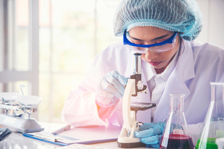 Woman scientist hand write note information in medical lab look at science microscope medical test, research biology chemistry. Asian Females technician laboratory analyzing blood test pharmaceuticalの写真素材