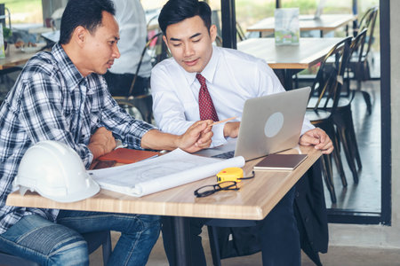 Contractor construction engineer meeting talking together on architect table at construction office site. Businessman engineer manager discuss with foreman team builder look at plan blueprint laptopの写真素材