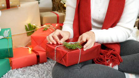 Close up woman hands wrap present gift in cozy living room. Woman wrapping christmas gift box under xmas tree. Asian woman decor bauble ball christmas tree in xmas holiday winter seasonal celebrationの写真素材
