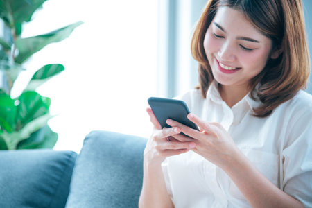 Asian woman holding smartphone with E-commerce Shopping online website Reading Online Article, Blog, vlog. Young Woman hands holding phone technology lifestyle. Happy Woman using digital smart phoneの写真素材