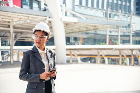 Civil women engineer wear safety white hard hat make a phone call in modern city. Young asian woman at construction site industry. Female engineer civil engineering with hard hat using smartphone.の写真素材