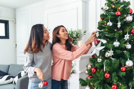 Two Women siblings using hands decorate Christmas tree red ball, bauble, snow flake. Close up hands holding red ball bauble decorate. Asian woman friends decor bauble ball christmas tree xmas holidayの写真素材