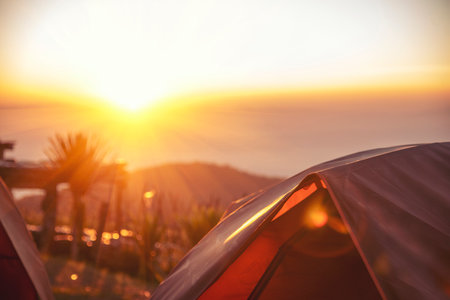 Tent Camping trip outdoor hiking mountain hill. Tent camp in nature background with sunrise on top of mountain. Picnic tent green nature campground in forest. Adventure Travel wildness flare sunlightの写真素材