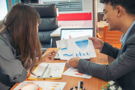 Two businesspeople meeting team discuss using laptop look at financial graph chart in office desk. Two young businessman reading Planning analyze marketing infographic. Partners team working togetherの写真素材
