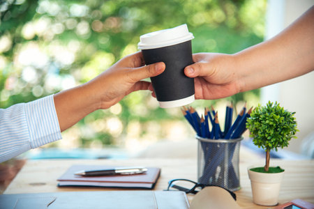 Close up hands business woman colleague drink coffee at office desk together. Friendship teamwork hold caffeine hot tea cup freshness lifestyle. Businesspeople give coffee cup to team active drinkingの写真素材