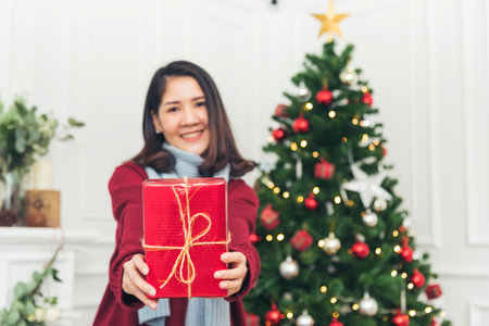 Woman surprise got present gift box on christmas eve. Asian woman holding christmas gift box under xmas tree with smiling face. Woman hands wrap present gift. Merry christmas happy new year conceptの写真素材