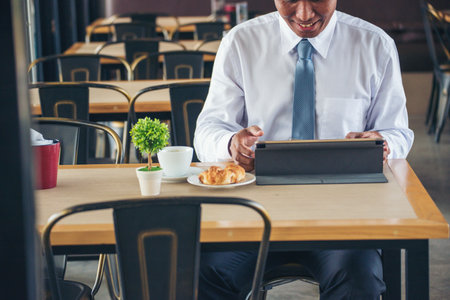 Businessman using smart digital tablet at office desk via wireless internet technology working online. Asian handsome man hold smart tablet use gadget check news. Freelance business person technologyの写真素材