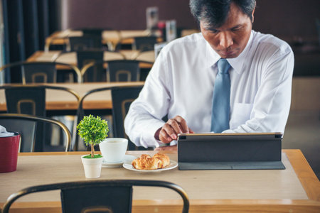 Businessman using smart digital tablet at office desk via wireless internet technology working online. Asian handsome man hold smart tablet use gadget check news. Freelance business person technologyの写真素材