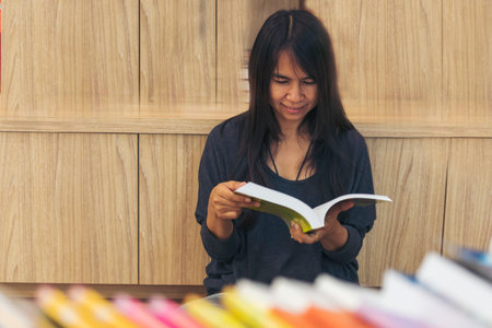 Asian woman holding book reading at bookshelf in university library. Young woman relaxation read...