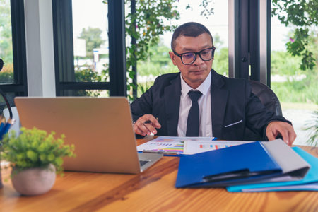 Asian Businessman using laptop at office desk. Man hands typing computer keyboard reading financial graph chart Planning analyzing marketing data. happy Asian business men people working office firmの写真素材