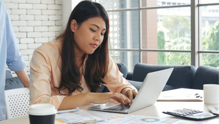 Asian Female freelance using laptop at home office desk. Woman reading financial graph chart Planning analyzing marketing data. Asian female people working office firm with business stuff, coffee cupの写真素材