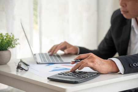 Asian businessman hands calculating number, graph, chart audit planning accountancy on business report. Asian professional Business man hands using calculator counting tax financial bill. Tax audit Finacial concept.の写真素材