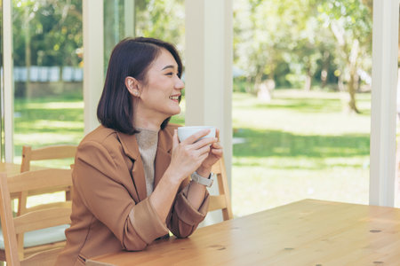 Beauty woman drinking black coffee in coffee shop holding freshness cup. Coffee lover. Asian Woman drink black coffee hand holding cup at green garden cafe. Young woman smile face love drink coffeeの写真素材