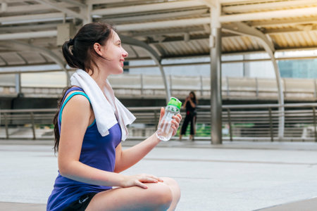 Women drinking water bottle running exercise in modern city wear wellness sportswear outside. Young woman workout outdoor exercising on bright sunny outside. Healthy wellness lifestyle woman conceptの写真素材