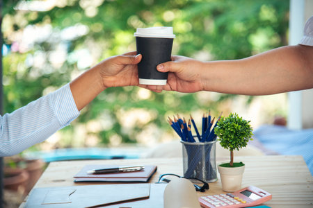 Close up hands business woman colleague drink coffee at office desk together. Friendship teamwork hold caffeine hot tea cup freshness lifestyle. Businesspeople give coffee cup to team active drinkingの写真素材