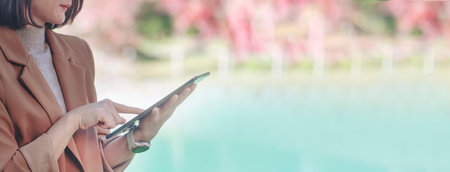 Banner Asian woman hands using digital tablet shopping online at lake autumn park. Panorama Female...