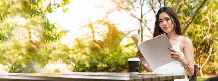 Banner woman holding book reading magazine at green park natural garden. Young woman relaxation read open book self study. Happiness University women smiling. Women sit in green park with copy spaceの写真素材